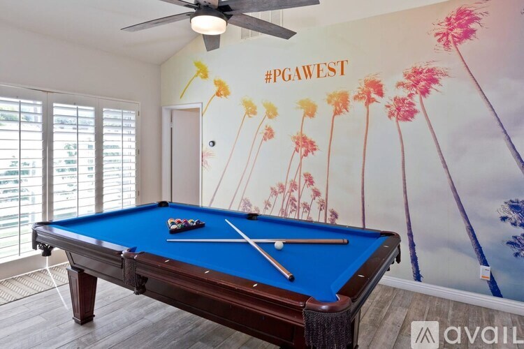 A pool table in a room with a wall mural of palm trees and the hashtag #PGAWEST.