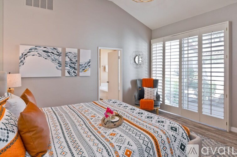 A bedroom with a bed covered in a patterned comforter and a wall hanging artwork.