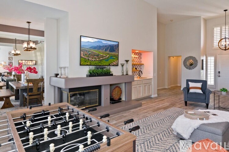 A foosball table is in the middle of a living room with a fireplace and a painting hanging above it.