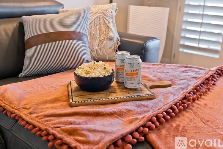 A black bowl filled with popcorn sits on a wooden tray on a leather couch.