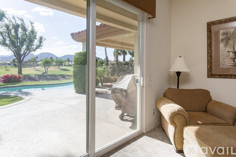 A living room with a couch and a lamp with a view of a pool and trees outside.