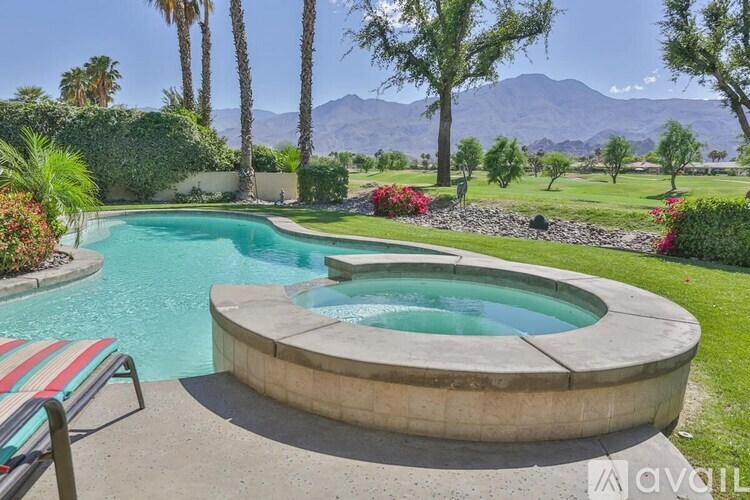 A pool with a hot tub in the middle of a garden with mountains in the background.