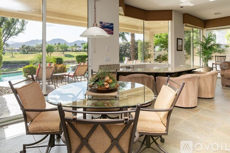A glass dining table surrounded by chairs in a room with a view of the outdoors.