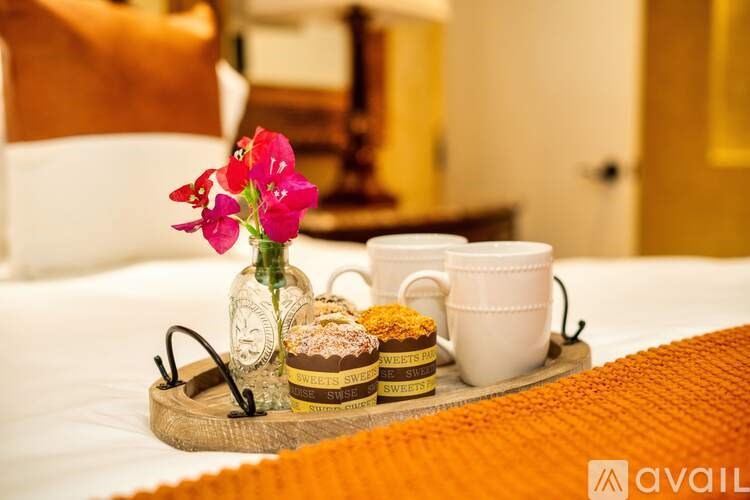 A tray with a cup, a jar of cookies, and a vase with flowers is on a bed.