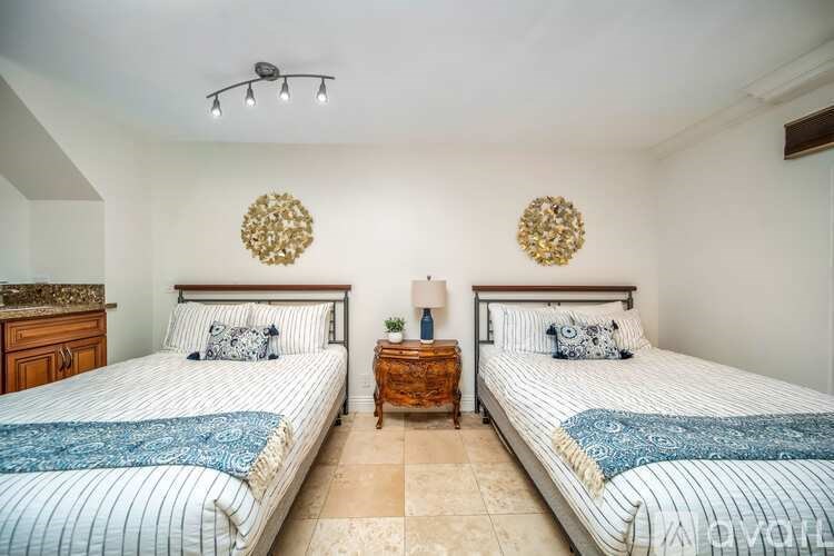 Two twin beds with blue bedspreads in a room with two wall sconces.