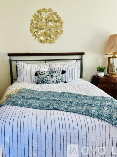 A bed with a blue and white striped comforter and a gold decorative piece on the wall.