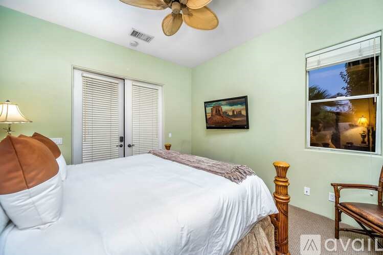 A bedroom with a bed, a ceiling fan, and a painting on the wall.