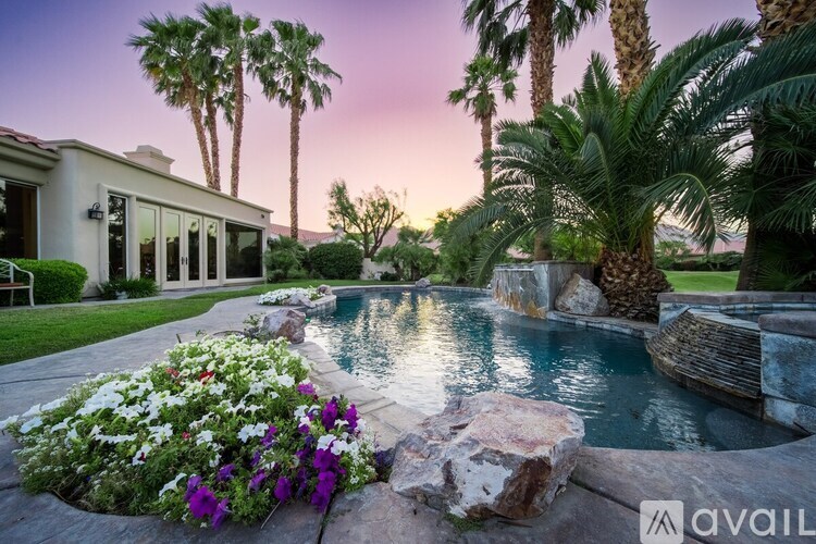A pool surrounded by rocks and plants with a house in the background.