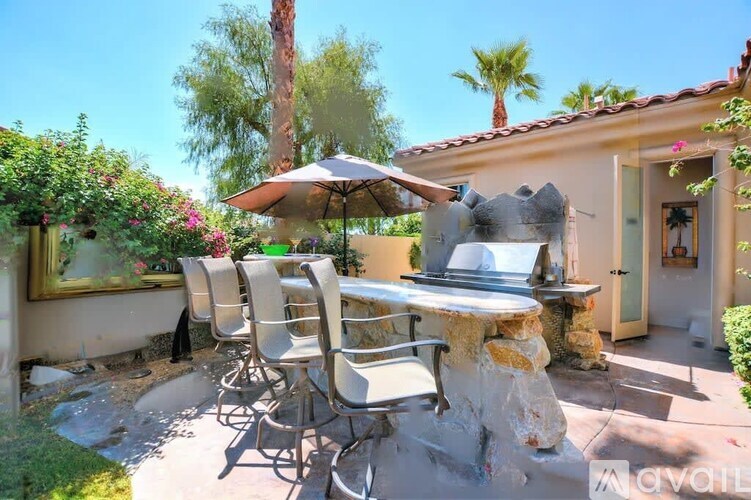 A patio with a table and chairs is surrounded by greenery.