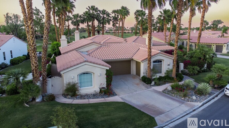 A house with a red tile roof is surrounded by palm trees.