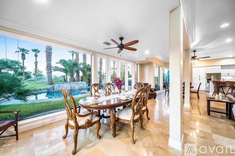 A dining room with a table set for six with a view of a pool and palm trees.