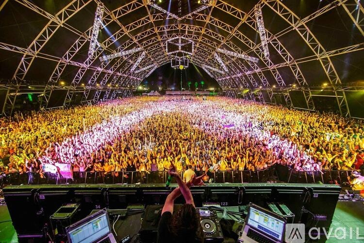 A DJ mixes music in front of a large crowd at a concert.