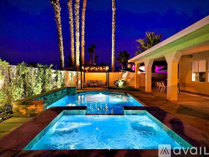 A pool with a waterfall and a lit up patio area.