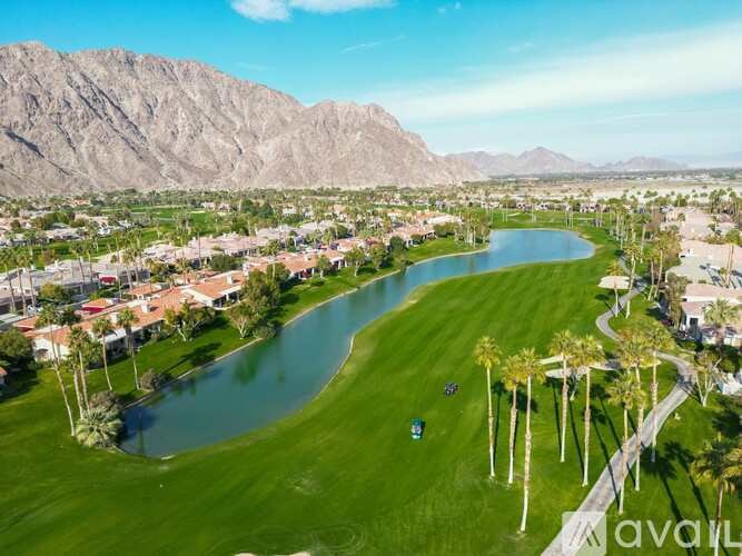 A golf course with a lake and palm trees in the foreground and mountains in the background.