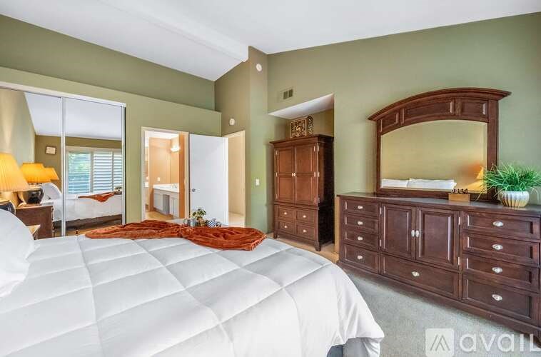 A bedroom with a large bed, a dresser, and a mirror.