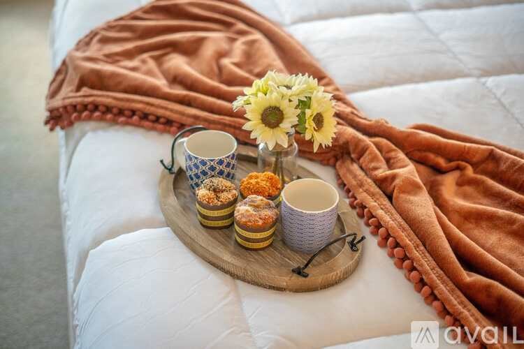 A tray with pastries, a cup, and a vase with flowers sits on a bed covered with a blanket.