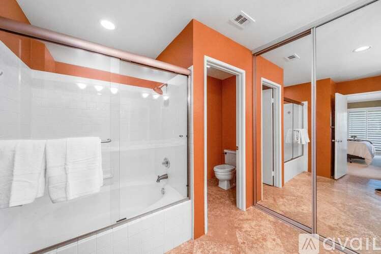 A bathroom with orange walls and a glass shower stall.