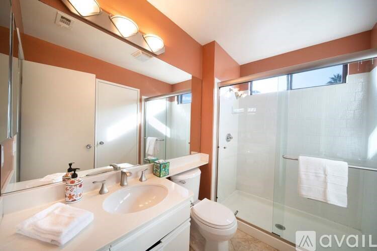A bathroom with a toilet, sink, mirror, and shower.
