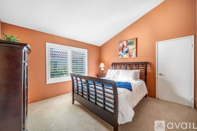 A bedroom with a bed, a window with blinds, a painting on the wall, and a door.