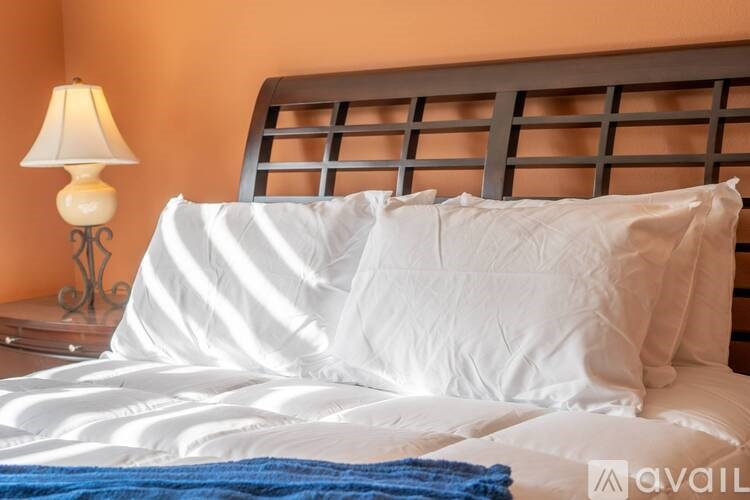 A bed with white pillows and a blue blanket is in front of a lamp.