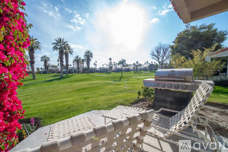 A patio with a grill and chairs overlooks a green lawn and palm trees.