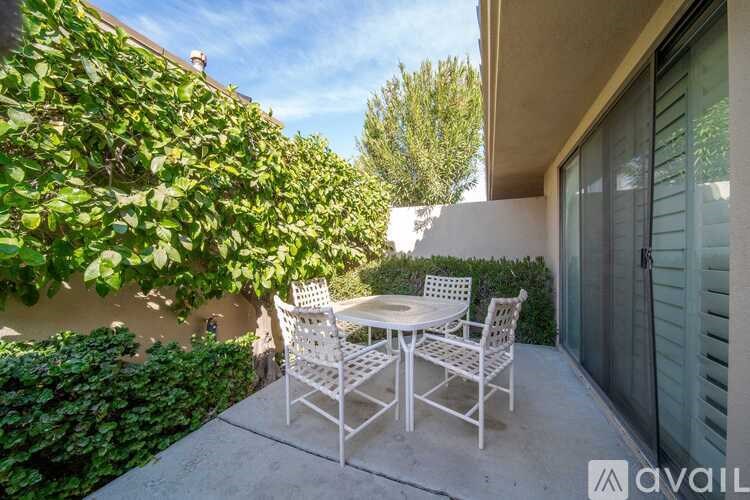 A patio with a table and chairs is surrounded by greenery.