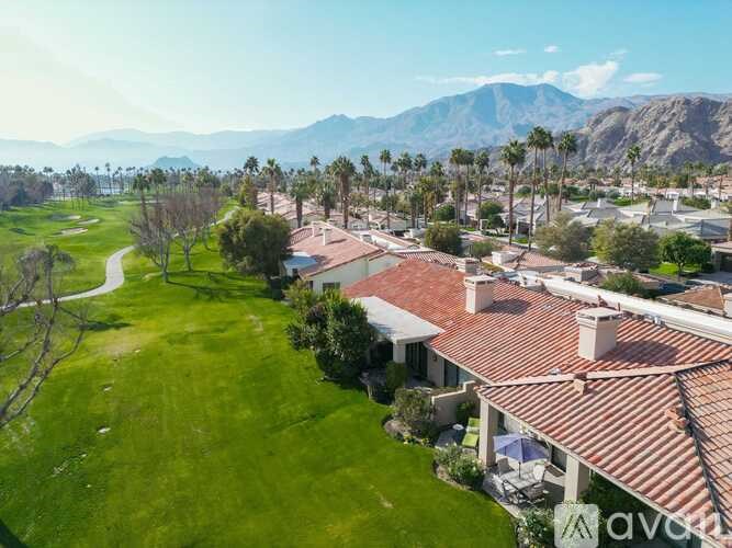 A house with a red tiled roof is surrounded by a green lawn and palm trees.