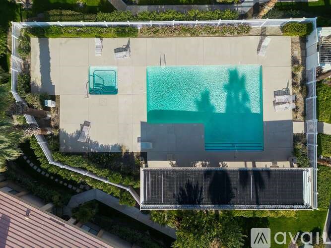An aerial view of a swimming pool surrounded by a concrete patio and a metal fence.