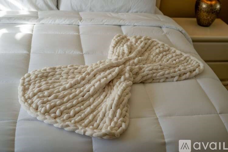 A white knitted blanket is draped over a white bed.