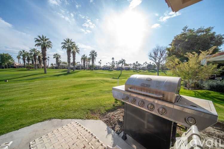 A large outdoor grill is in the foreground of a sunny backyard.