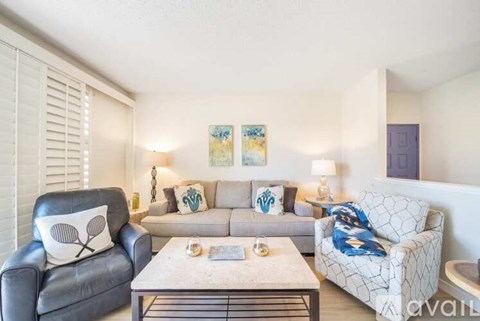 A living room with a grey leather chair, a white patterned couch, and a coffee table.