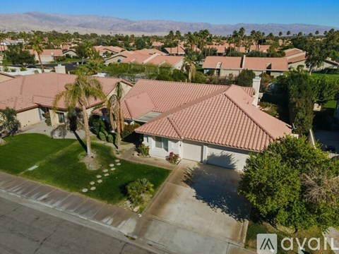 A house with a red tiled roof is surrounded by other houses and palm trees.