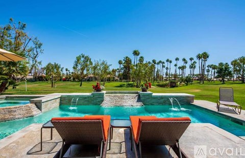A pool with two lounge chairs and a table is surrounded by palm trees.