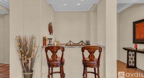Two wooden chairs are placed in front of a table with a vase of dried plants on the left.