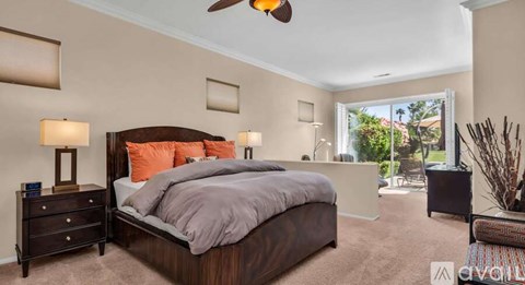 A bedroom with a large bed, a ceiling fan, and a view of the outdoors through a window.