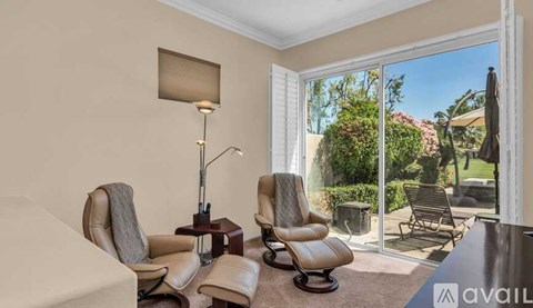 A living room with a large window and a view of a garden and patio area.