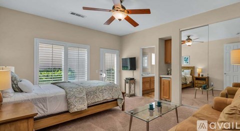 A bedroom with a bed, a couch, a ceiling fan, and a television.