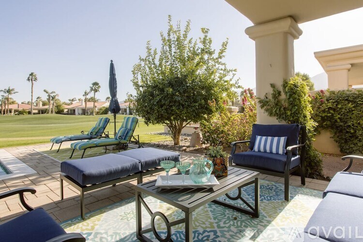 A patio with blue cushions and a table with a glass top.