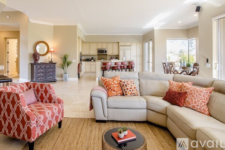 A living room with a red and white patterned chair and a grey couch with orange pillows.