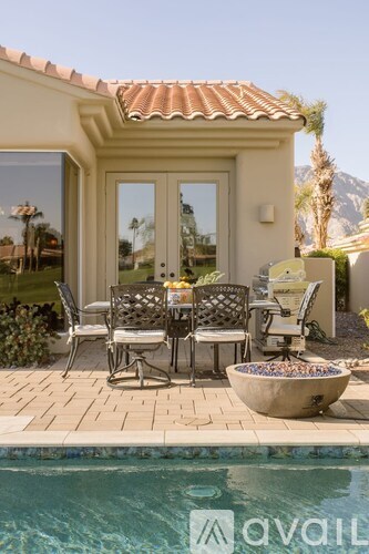 A poolside table with chairs and a bowl of stones is in front of a house.