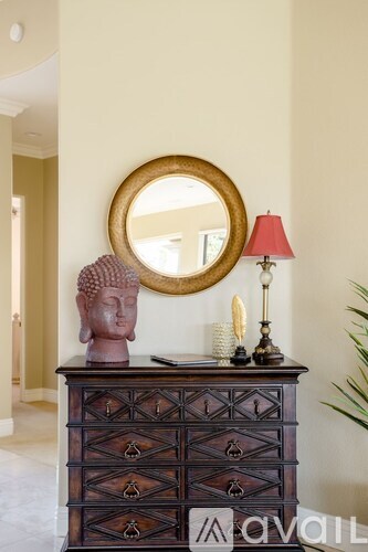 A wooden chest of drawers with a round mirror above it and a red lamp beside it.