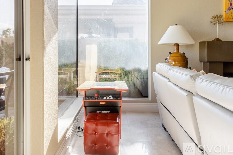 A red chair sits in front of a window in a white room.