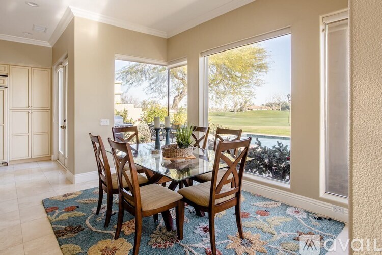 A dining room with a table and chairs and a view of a lawn outside.