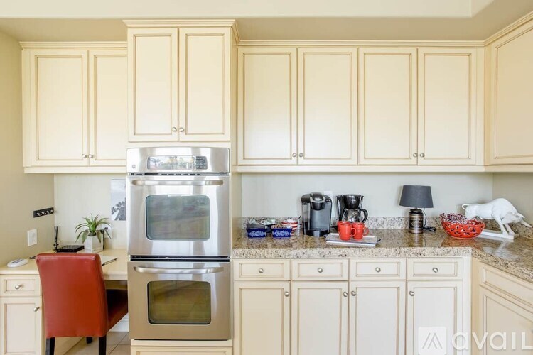 A kitchen with a stainless steel oven and a red chair.