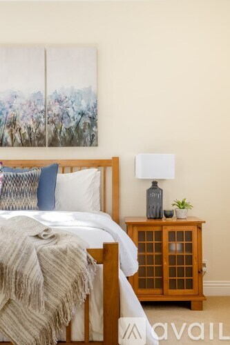 A bedroom with a bed, a nightstand with a lamp, and a painting on the wall.