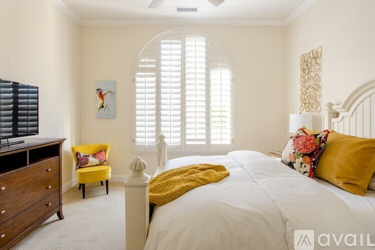 A bedroom with a large bed, a yellow chair, and a painting on the wall.