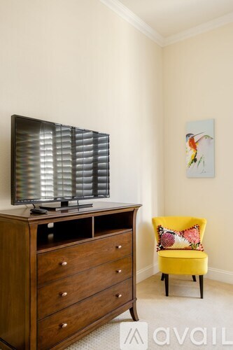A yellow chair sits in front of a wooden cabinet with a television on top.