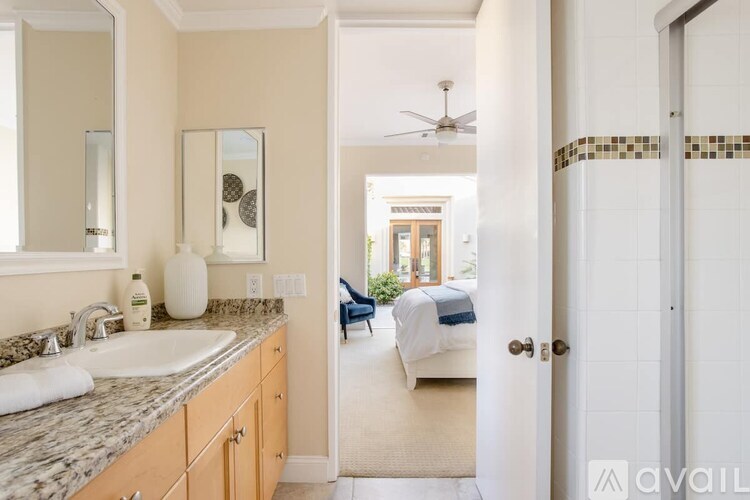 A bathroom with a sink, mirror, and a bedroom in the background.