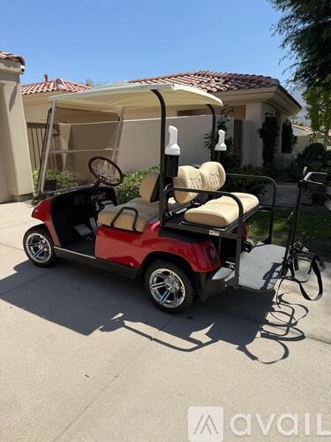 A red and black golf cart with a canopy and two seats is parked on a driveway.