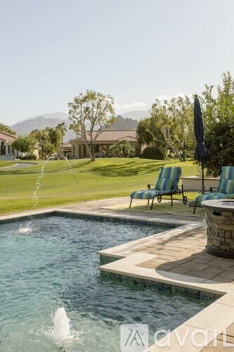 A pool with a waterfall and a patio with chairs.